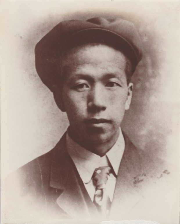 Sang (Sam) Chun is looking at the camera. He is wearing a beret-like hat, jacket, shirt and tie. He looks like he is smiling slightly.