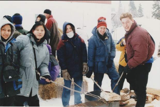 A number of young people dressed in winter gear roasting bannock over a fire. The activity was part of the 1999 Trappers' Festival.