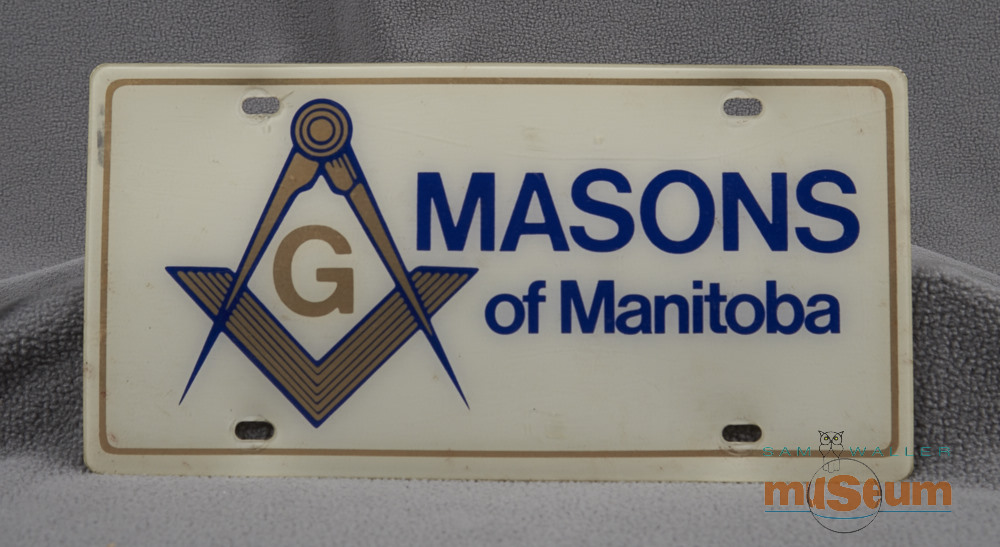 Plain white licence plate with blue lettering for the Masons of Manitoba and a gold symbol lined in blue.