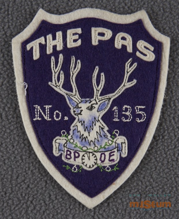 Purple shield shaped patch with white trim, lettering and elk at centre. In white on patch is written The Pas, no.135.