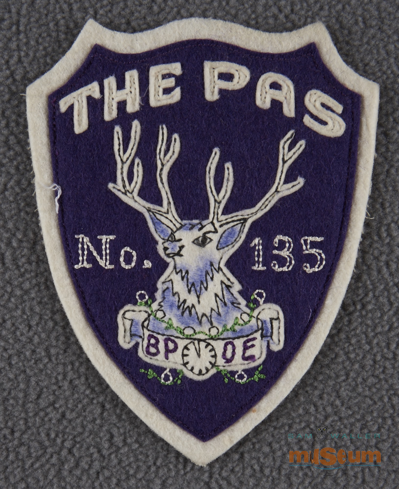 Purple shield shaped patch with white trim, lettering and elk at centre. In white on patch is written "The Pas, no.135".