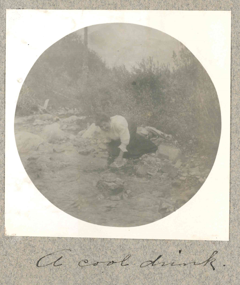 Photo of Isabella at edge of creek scooping a drink of water.