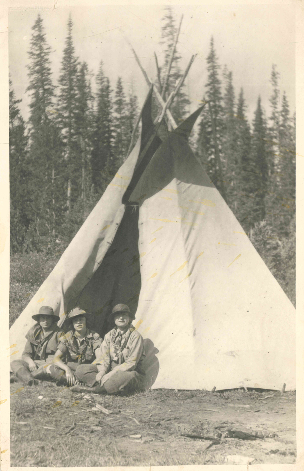 Photo of Dorothy Lougheed in between 2 other girls all dressed in scout clothes in front of a teepee.