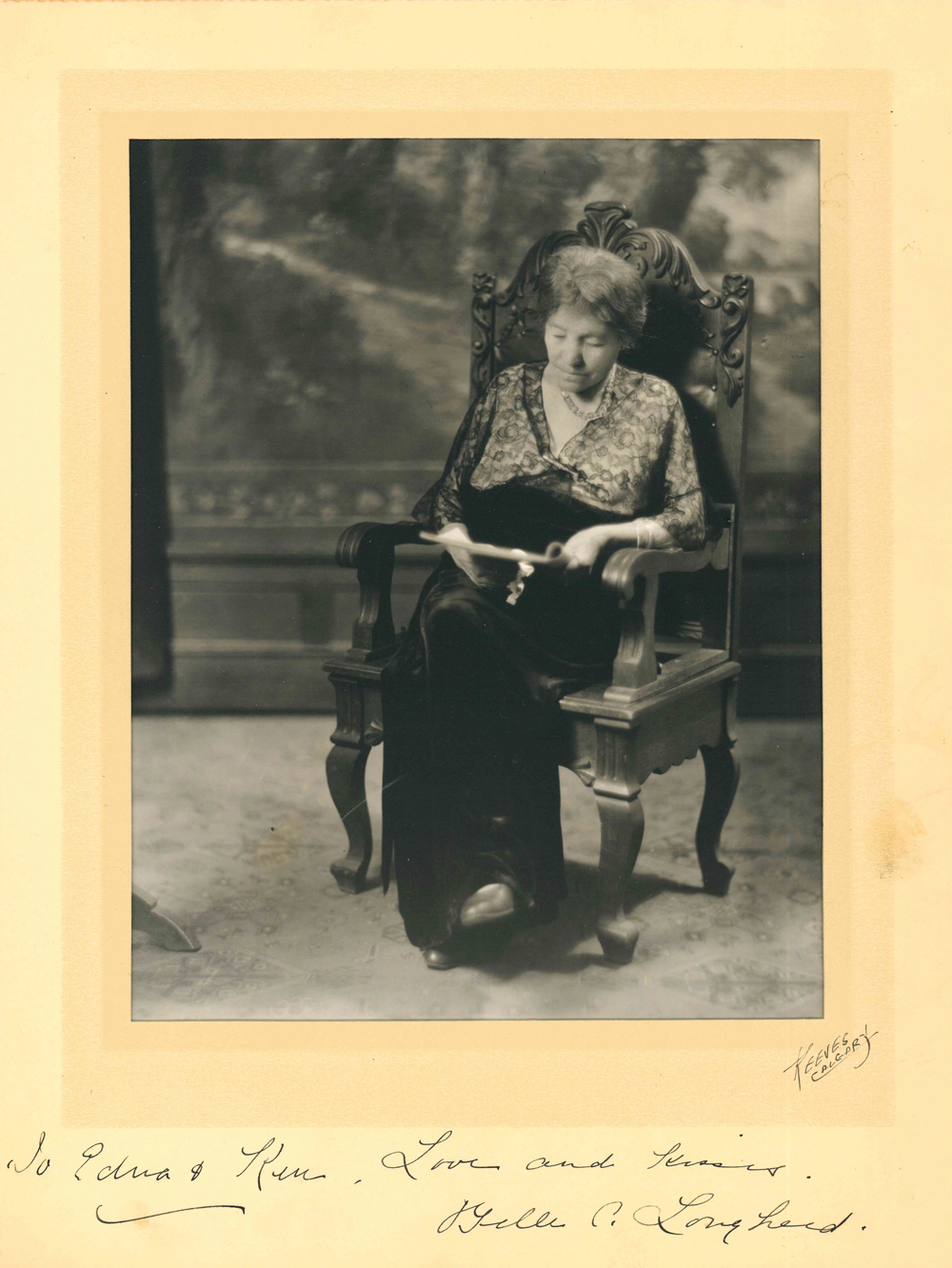 Studio photo of Belle as elderly woman seated in a chair reading.