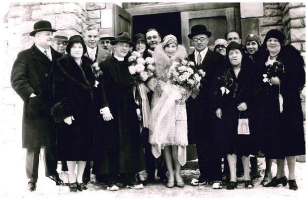 Group photo from Clarence Lougheed's wedding in front of a church door in Banff, Isabella stands in front row next to Clarence.