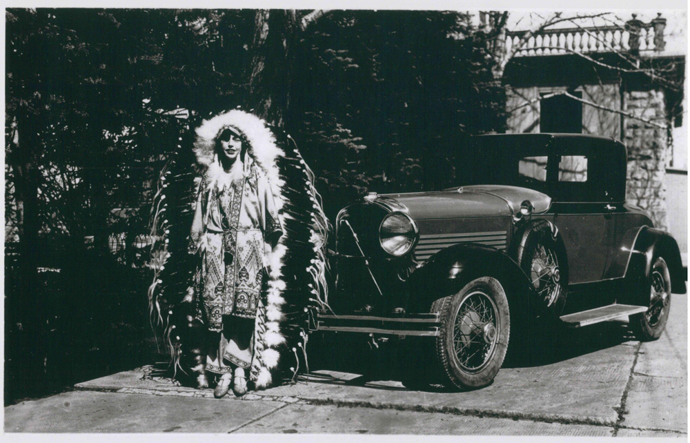 Photo of Dorothy Lougheed in large feathered headdress beside car at Beaulieu