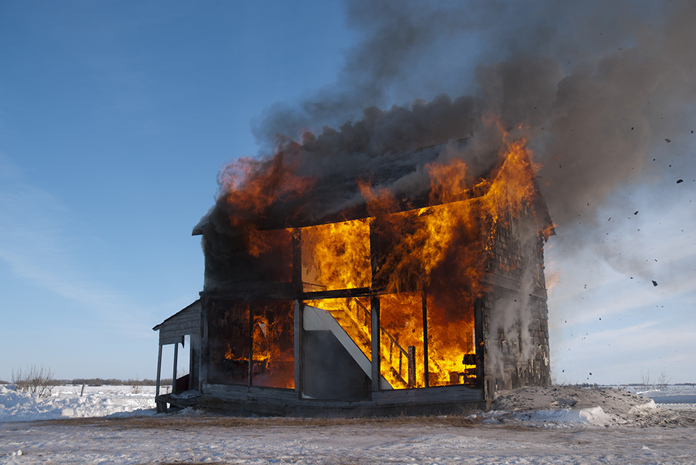 Video still of half a farm house cut in cross section, being consumed by fire.