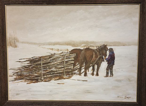 A person with two horses and a sled full of logs on a snowy field.
