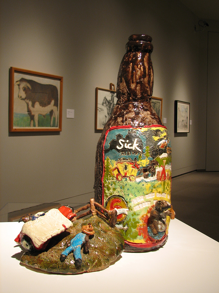 Sculpture en argile d’une grande bouteille de bière et, à côté, un petit fermier endormi dans un champ.