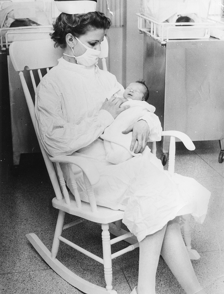 Nurse holding a baby in a rocking chair in a hospital in a black and white photo.