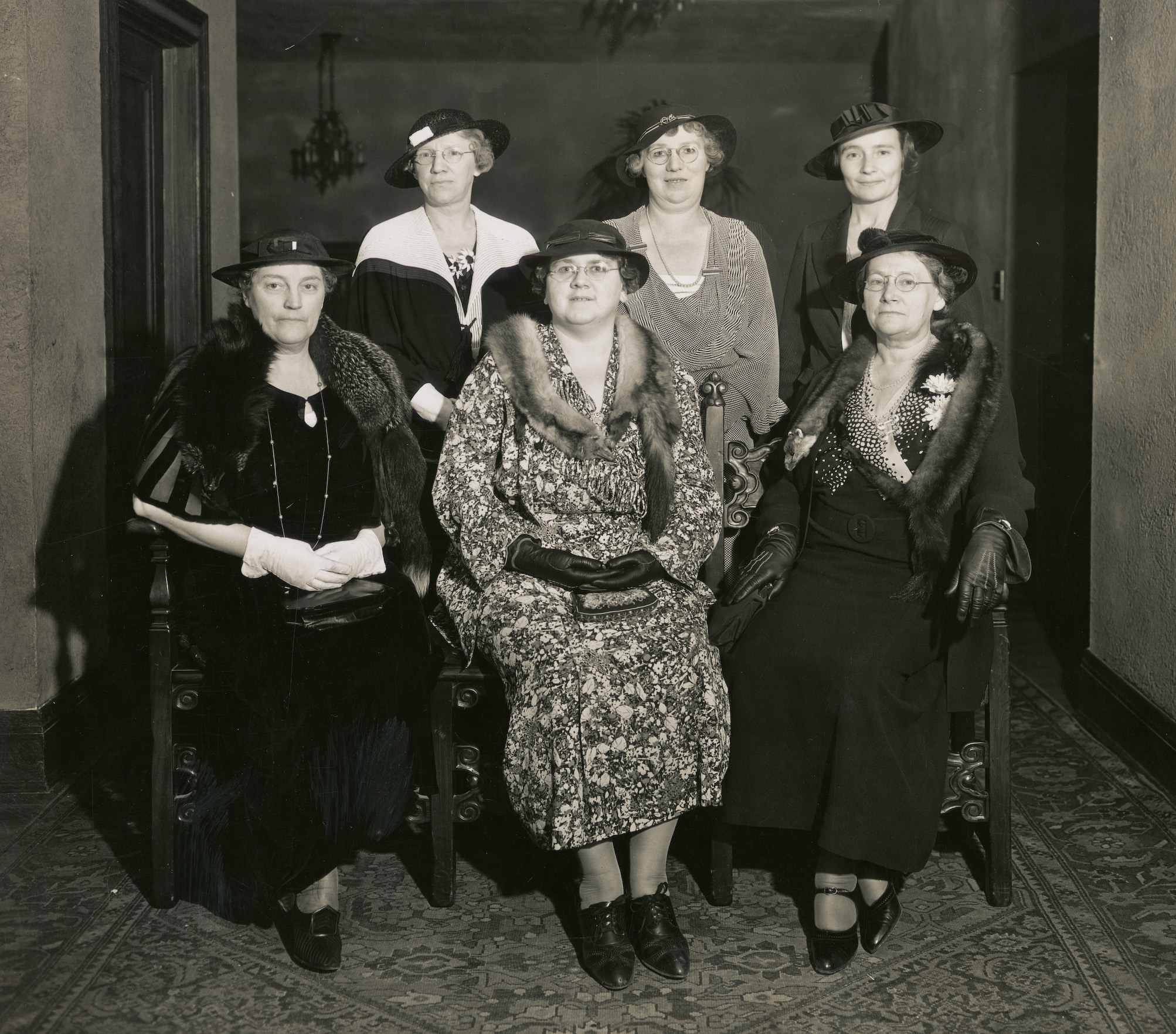 Formal black and white portrait of six hospital staff. Three of the women are seated in chairs while another three women pose behind them.