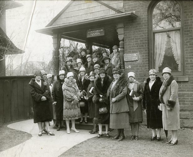 Group of fashionably dressed women in winter coats and hats stand outside the Women’s College Hospital in a black and white photo.