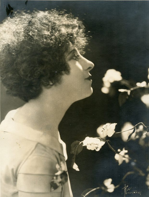 Balck and white profile portrait of Jeanne Mignolet standing among flowers.