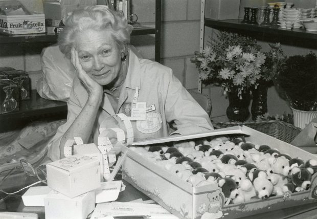 Grace Tatum sitting at a table in a black and white photo, surrounded by paper raffle tickets and a box of teddy bears.
