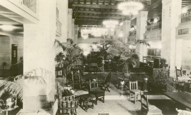 Elegantly furbished lobby with varied seating arrangements, potted palms and chandeliers in a black and white photo.