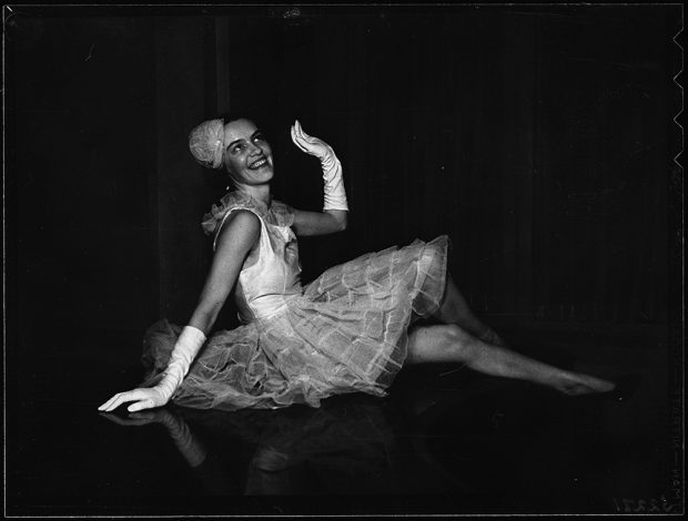 Peggy Beal seated on floor poses in tutu costume and gloves in a black and white photo.