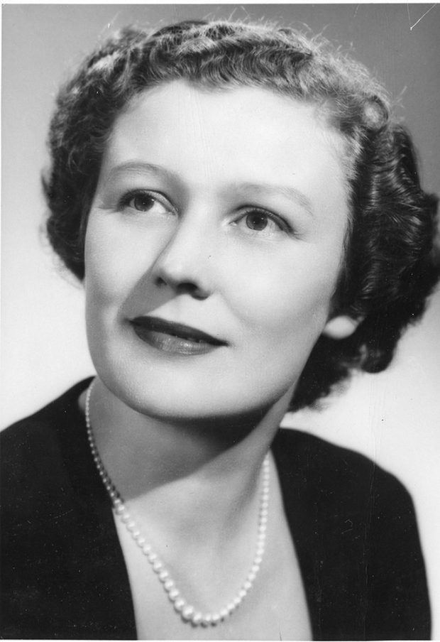 A black and white portrait of a delicately smiling woman wearing pearls.