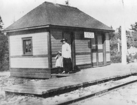 Cole Station with a woman and child standing in front of it