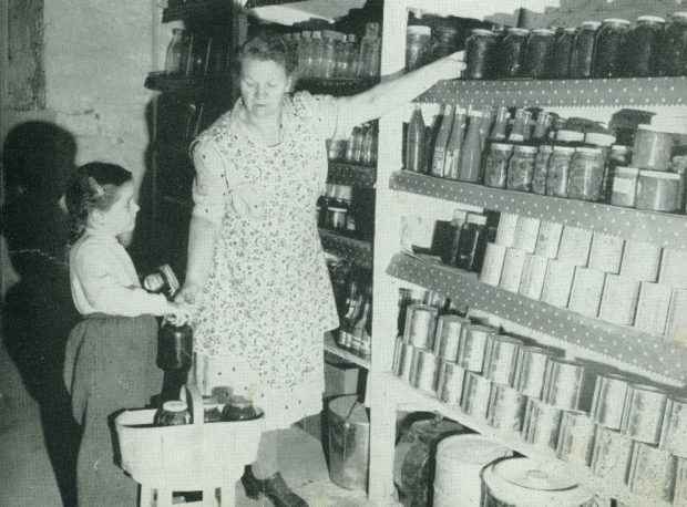A woman and a little girl put away canned goods in a cold room