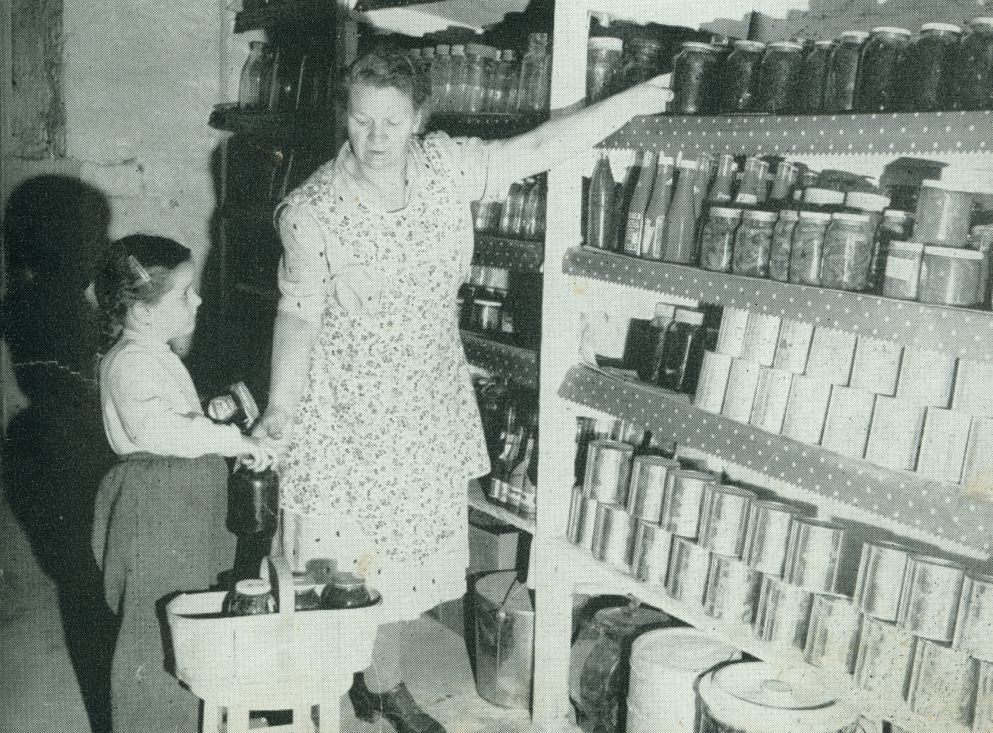 A woman and a little girl put away canned goods in a cold room