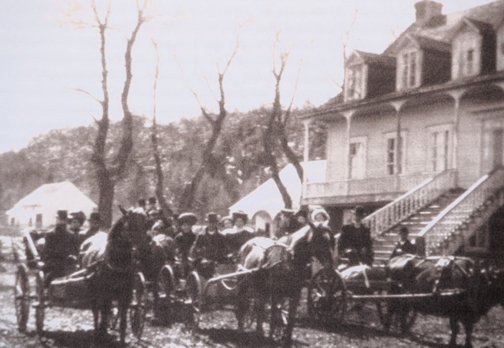 Three horse-drawn carriages with people in front of a house