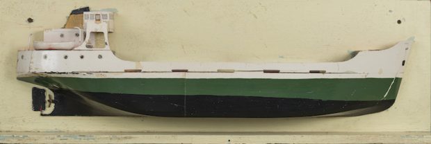This colour photograph shows a model of the Mont St-Martin coaster. The model is a cross-section. The hull features a black and a green stripe. The upper portion and cabins are painted white. The ship’s propeller is visible in the back.