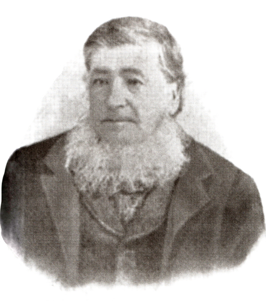 A black and white portrait of a man. The picture is cut at the bust line. On it we see an aged man with short hair sporting a white beard under his chin. The man is wearing a jacket.