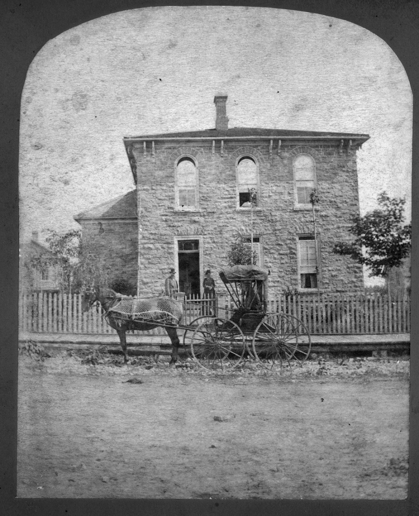 Black and white photograph of a stone house with a horse and buggy in the foreground.