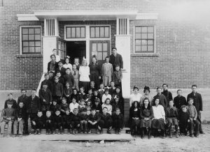 Grande photo d'école d'enfants assis sur le perron de l'école en briques à deux étages.