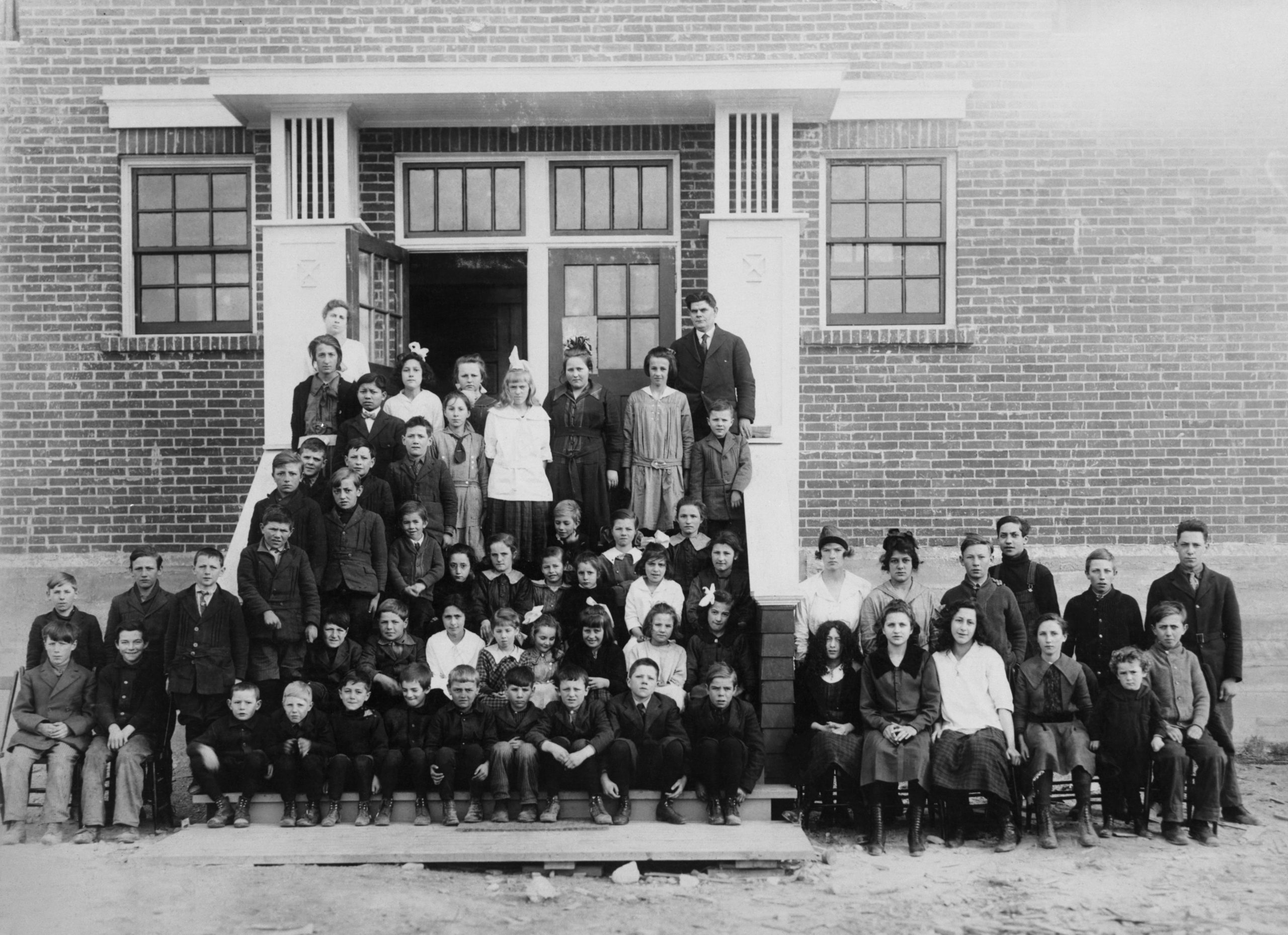 Large school photo of children sitting on the front steps of the two story brick school.