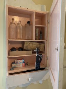 Medicine chest with five compartments holding three bottles, two shaving brushes, prescription sunglasses in original box, two boxes of gauze and bandages and salves.