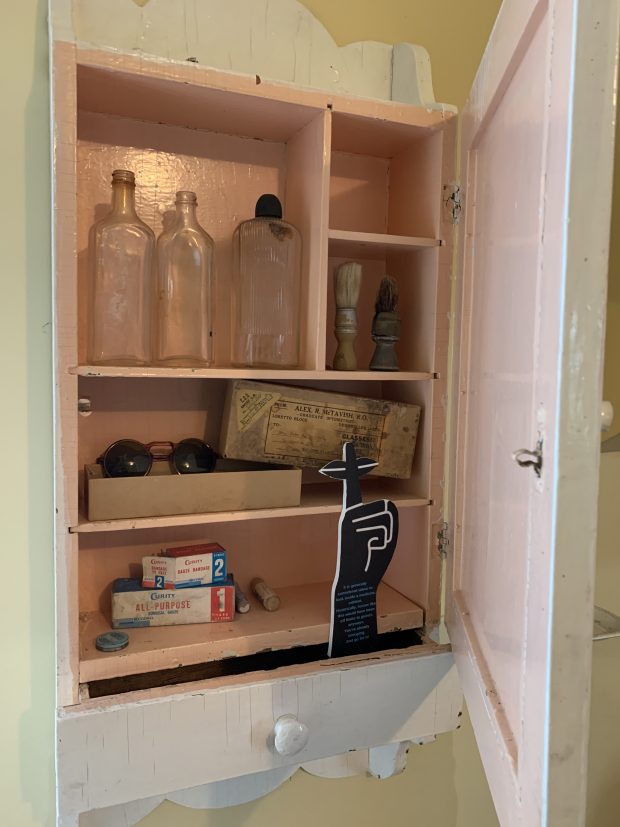 Medicine chest with five compartments holding three bottles, two shaving brushes, prescription sunglasses in original box, two boxes of gauze and bandages and salves.