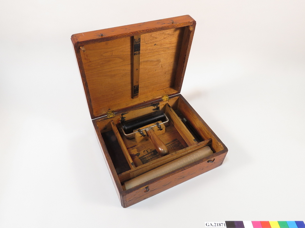 Wooden covered box with roller and ink and paper supplies for copying.