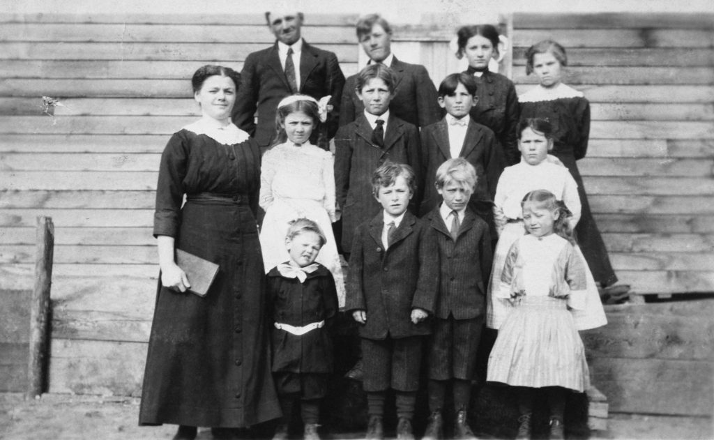Two adults with eleven children standing outside a house.