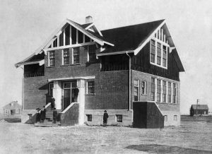 Two story brick school with two outbuildings in background with six children in front.