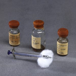 Trois fioles à vaccin avec seringue sur un tampon d’ouate, vers 1952.