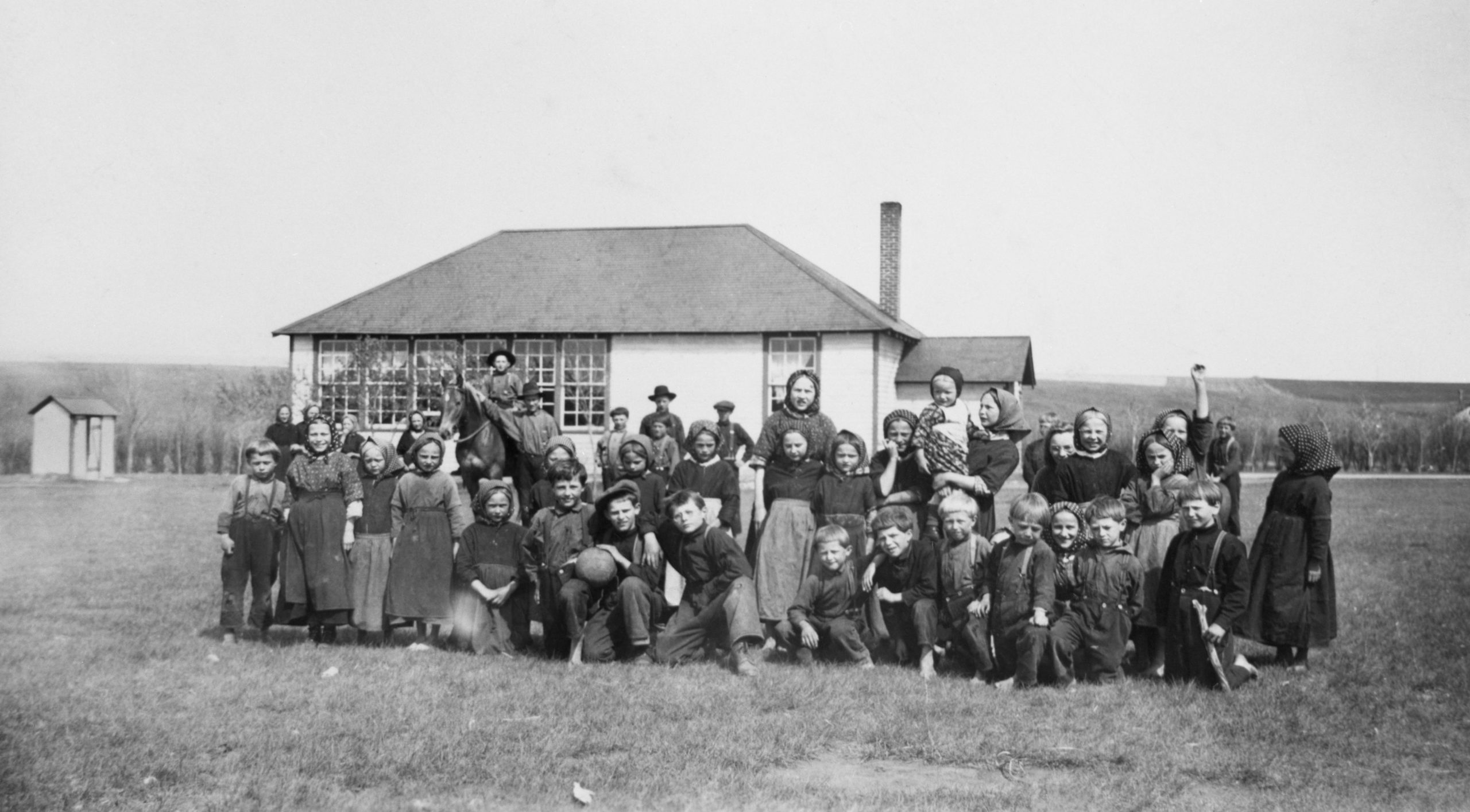 Class in front of school, outhouse in background.