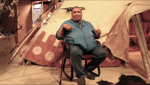 Adrian Wolfleg in front of a large tipi at Glenbow Museum