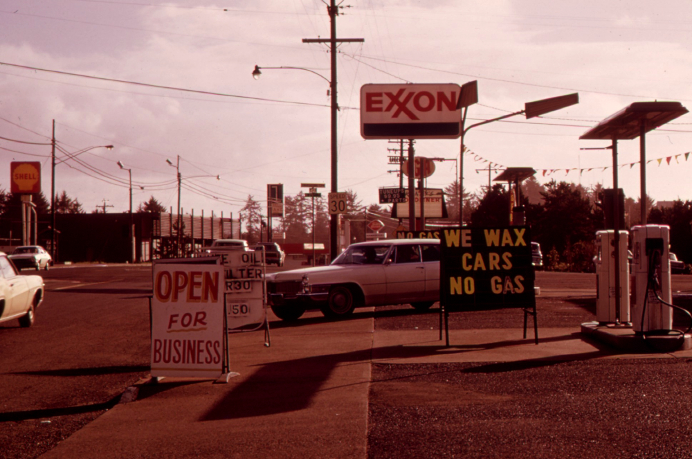 Colour photograph of a car pulling out of an Exxon gas station. A sign in front of the station reads “WE WAX CARS / NO GAS”