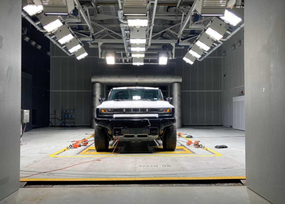 Colour photograph of a large truck plugged into a wall outlet. The truck is mounted on a test stand in the center of a large industrial room.
