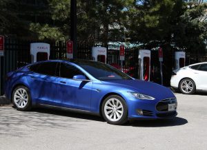 Photo couleur d'une voiture électrique garée à une station de recharge. Panneau de la station : TESLA 