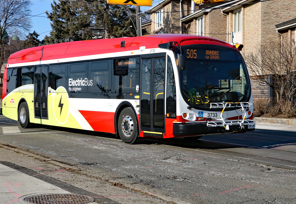 Colour photograph of a bus on a suburban street. Signage on the side reads “Electric Bus”