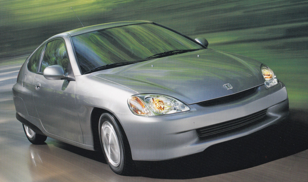 Colour photograph of a streamlined car driving down a forested road. The background had been edited to add speed lines.