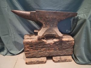 Modern colour photograph of a large anvil on a worn wooden stand.