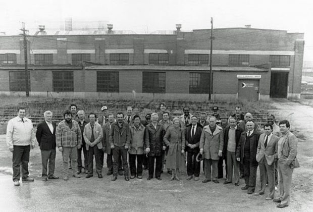 Black and white archival photograph of about 25 people posed in front of the John Street Roundhouse.