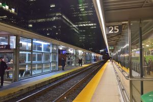 Colour photograph of Platform 25 at Toronto’s Union Station. It is nighttime and there is an empty railway track with train platforms on either side. There are a few people on either platform.