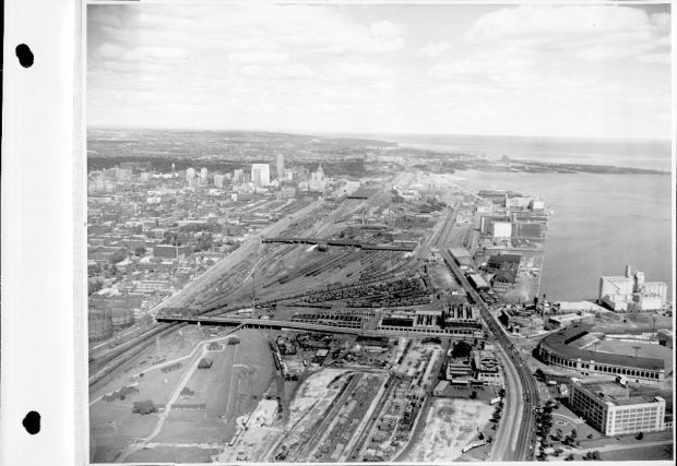 Black and white vintage aerial photograph. The centre of the photograph shows many railway tracks. The right bottom corner shows a baseball stadium. The left side of the photograph shows many buildings.
