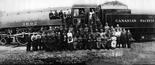 Landscape vintage photograph shows approximately 50 men posing in front of and in a large steam locomotive. The number “3002” is visible on the locomotive and “Canadian Pacific” on the tender. Illegible script is visible in the bottom of the photograph.