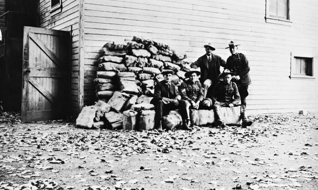 Three policemen and two other men in front of a pile of booze.