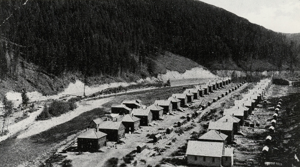 Deux longues rangées de chalets de mineurs à côté d'une rivière.